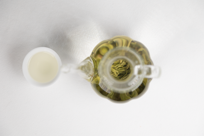 Top view of freshly brewed green tea with visible tea leaves in a glass teapot and a small cup on a white background, highlighting tea's natural antioxidant richness.