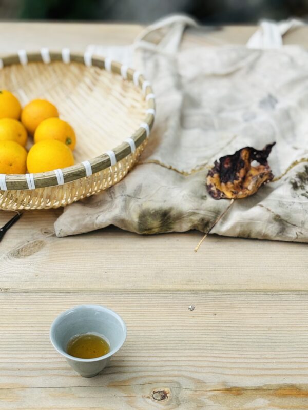A ceramic teacup and fresh oranges arranged on a wooden table, evoking a warm seasonal tea moment