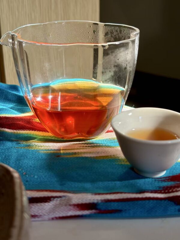 Amber-colored Wuyi rock tea in a glass cup, showing layered light, warm tones, and translucent clarity of the tea.