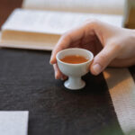 Person holding a small cup of warm Chinese tea during a quiet post-meal relaxation moment