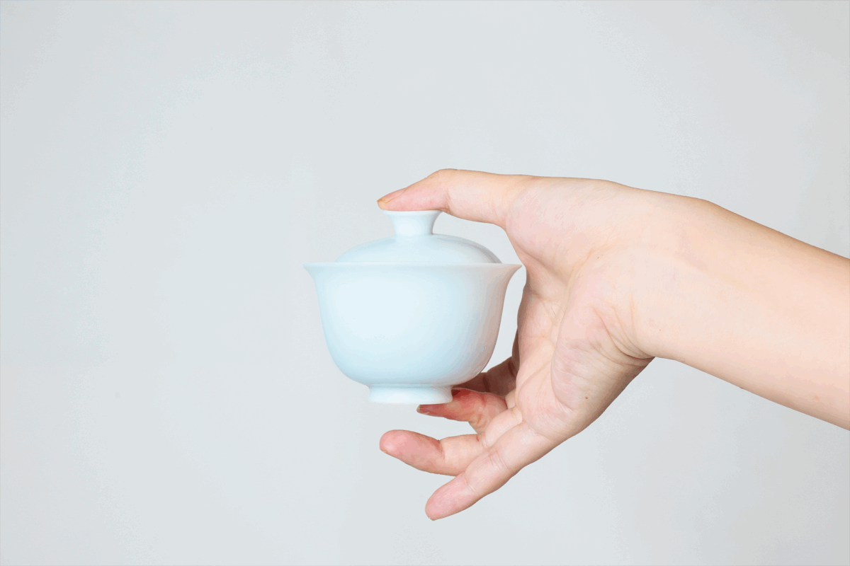 Instruction image showing correct gaiwan pouring in a portable porcelain gongfu tea set, including inner-wall pouring, comfortable grip, moderate opening, and natural tea flow