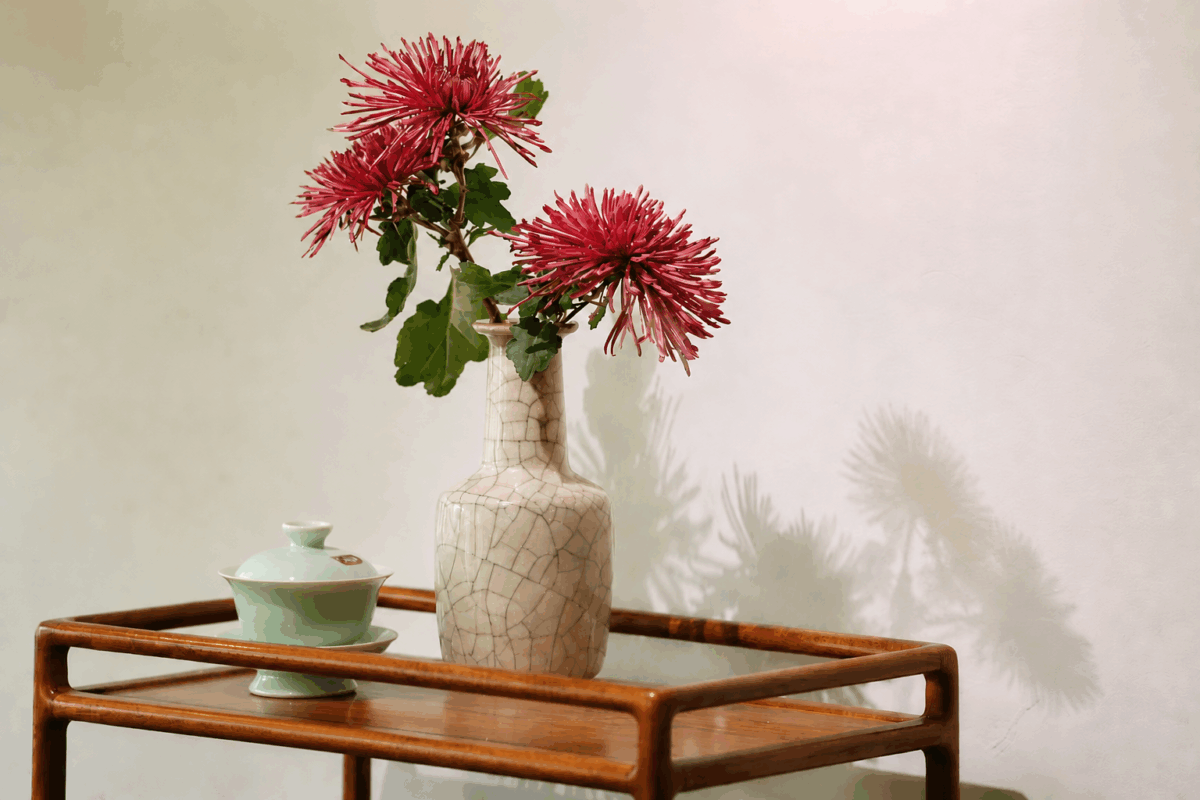 A Longquan celadon gaiwan on a wooden tea tray with flowers and soft shadows, showing Chinese celadon teaware in a daily tea ritual.