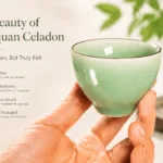 A hand holding a Longquan celadon tea cup, showing the smooth jade-like glaze and tactile feel of Chinese celadon teaware.