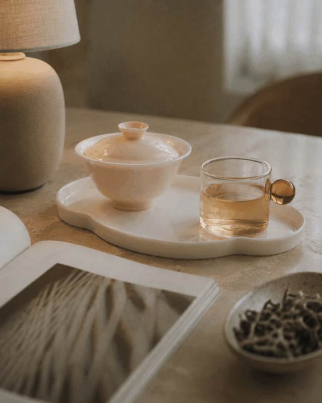 Jianyang Bai Mu Dan white tea in a warm reading scene with a pink gaiwan, glass cup, open book, and loose tea leaves.