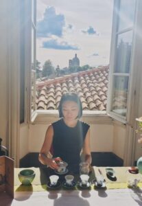 Ling Chen preparing Chinese tea beside an open window overlooking Milan