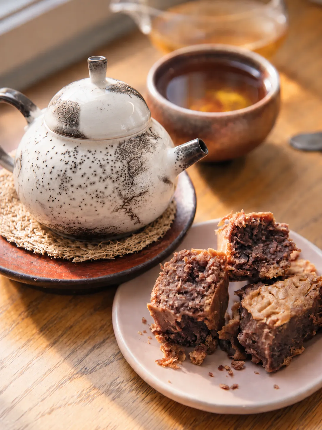 A ceramic teapot, cup of tea and pastries in warm light, representing tea, body awareness and sensory grounding during depression.
