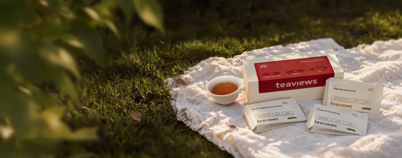 Teaviews Chinese black tea tasting box with three tea sachets and a cup of amber-coloured black tea arranged on a cream picnic blanket outdoors.